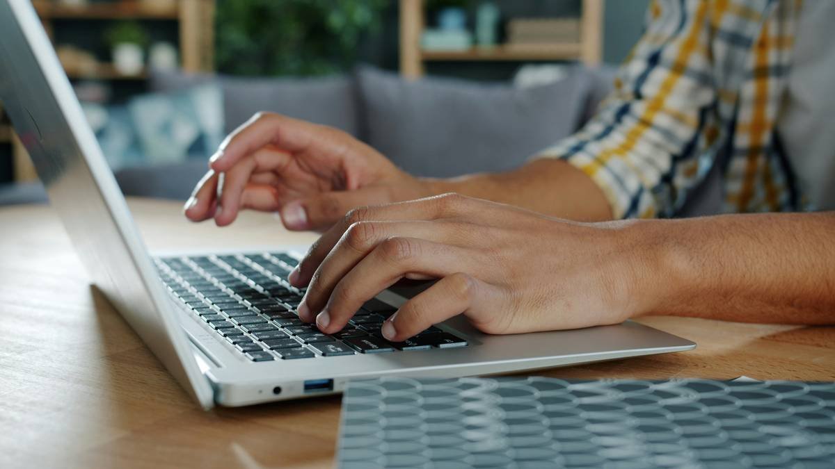 man's hands typing using laptop computer indoors at home, freelancer is working in apartment alone. People and devices concept.